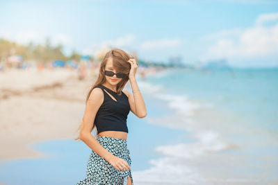 Side view of young woman standing at beach against sky