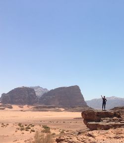 Woman standing on rock formation at desert against clear sky