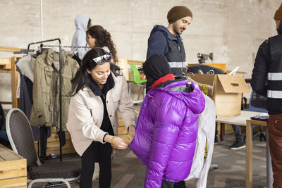 Woman assisting son while wearing padded jacket at recycling center