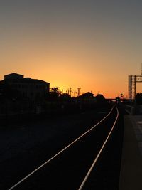 Railroad tracks by buildings against clear sky during sunset