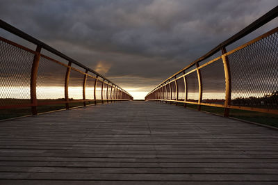 Boardwalk against cloudy sky during sunset