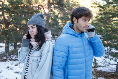 Couple talking on mobile phone while standing on snow covered field