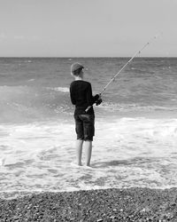 Rear view of boy standing fishing on the beach