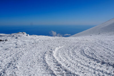 Snow covered land against clear blue sky