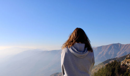 Rear view of woman looking at mountains against clear sky