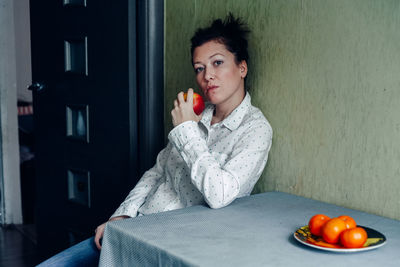 Portrait of beautiful woman holding apple while sitting at home