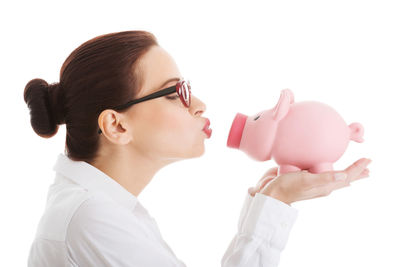 Smiling young businesswoman kissing piggy bank against white background