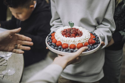 Midsection of boy giving fresh cake to woman at birthday