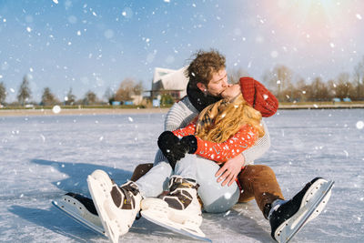 Couple kissing while sitting on snow covered land during winter