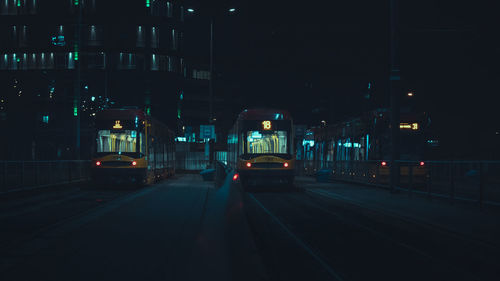 Illuminated railroad tracks by buildings in city at night