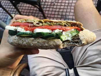 Cropped image of man having sandwich while sitting at outdoor restaurant