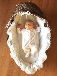 Directly above view of baby sleeping in wicker baby carriage on hardwood floor