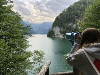 Rear view of woman looking through coin-operated binoculars against sea