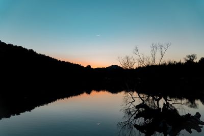 Silhouette trees by lake against sky during sunset