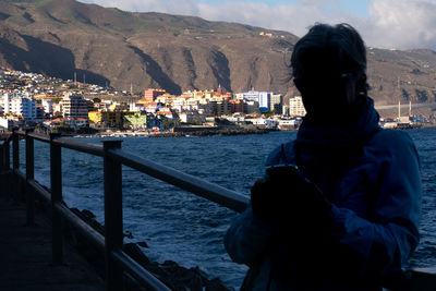 Portrait of man standing by sea against cityscape