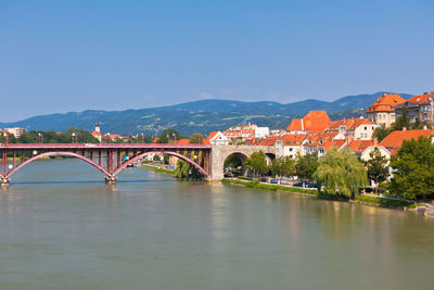 Arch bridge over river by buildings against clear blue sky