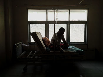 Rear view of man sitting on bed at hospital