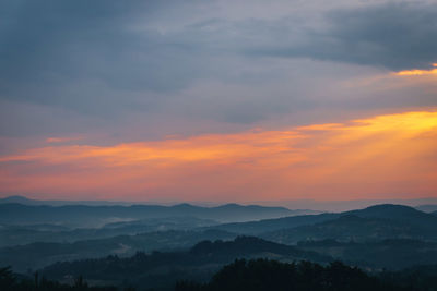 Scenic view of dramatic sky over silhouette mountains during sunset