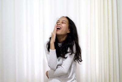 Beautiful young woman with eyes closed standing against curtain