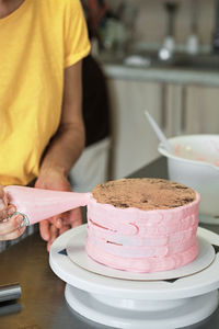 Woman spreads pink cream on cake with pastry bag, close-up. cake making process, selective focus