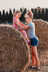 Teenage girl holding sister on hay bale