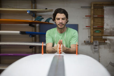 Concentrated worker adjusting fins on surfboard in workshop