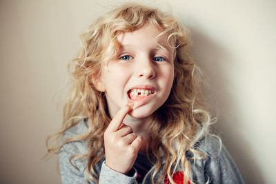 Portrait of cute girl showing missing tooth against wall