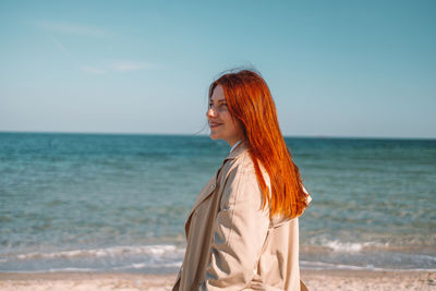 Young woman standing at beach against sky