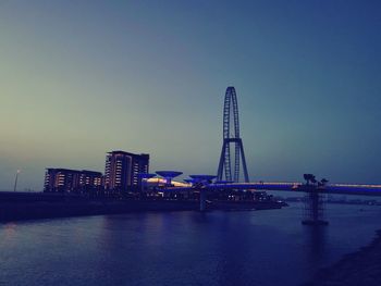 Bridge over river by buildings against sky at dusk