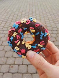 Cropped hand of person holding donut against street