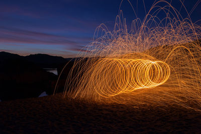 Light trails on beach against sky at night