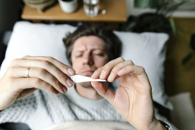 Man looking at thermometer lying on bed at home