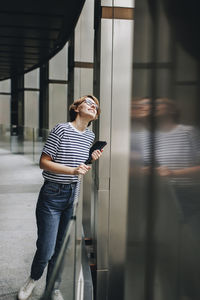 Woman holding tablet pc leaning on glass railing and looking up