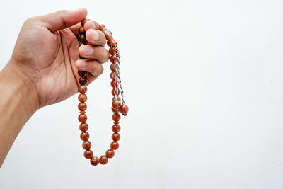 Cropped hand holding prayer beads over gray background