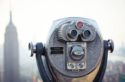 Close-up of coin-operated binoculars against buildings in city