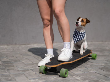 Low section of woman standing on skateboard with dog