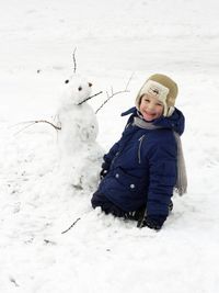 Portrait of cute boy kneeling by snowman during winter