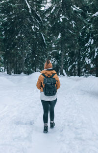Rear view of woman hiking on snowy path leading to moody forest in winter