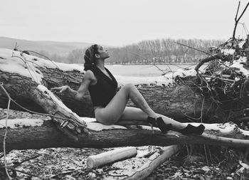 Portrait of young woman sitting on shore against sky