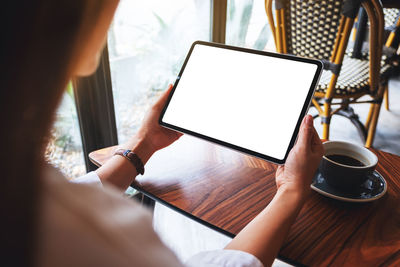 Mockup image of a woman holding black tablet pc with blank white screen with coffee cup on the table