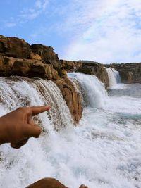 Close-up of hand splashing water in sea against sky