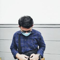 Young man looking away while standing against wall