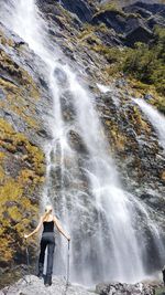 Full length of woman standing on rock by waterfall