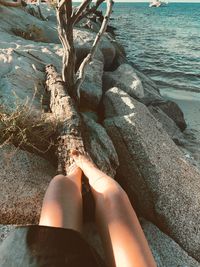 Low section of person relaxing on rock at beach