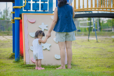Rear view full length of woman standing with baby girl by play equipment