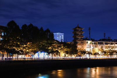 Illuminated buildings by lake against sky at night