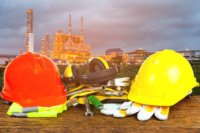 Close-up of protective workwear with hand tools on wooden table against oil factory during sunset