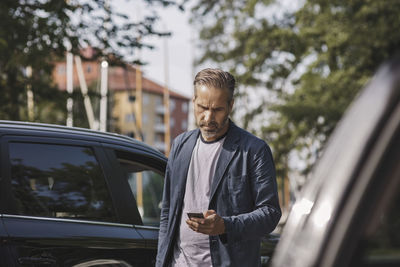 Businessman using smart phone while standing by cars at park