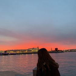 Rear view of woman by lake sky during sunset in city