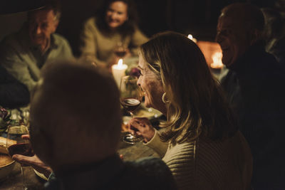 Smiling senior woman enjoying with male and female friends during candlelight dinner party